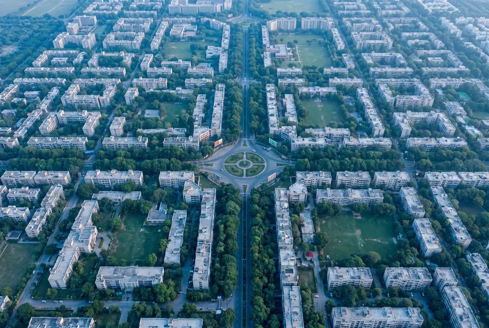 A planned Indian city from the air in morning light, tree-lined avenues dividing neat rectangular sectors of low-rise buildings.